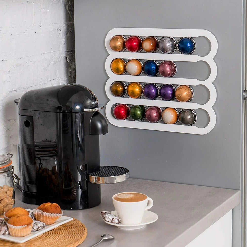 Black coffee machine with a cup of coffee on a counter, next to a wall-mounted holder with colorful coffee capsules.