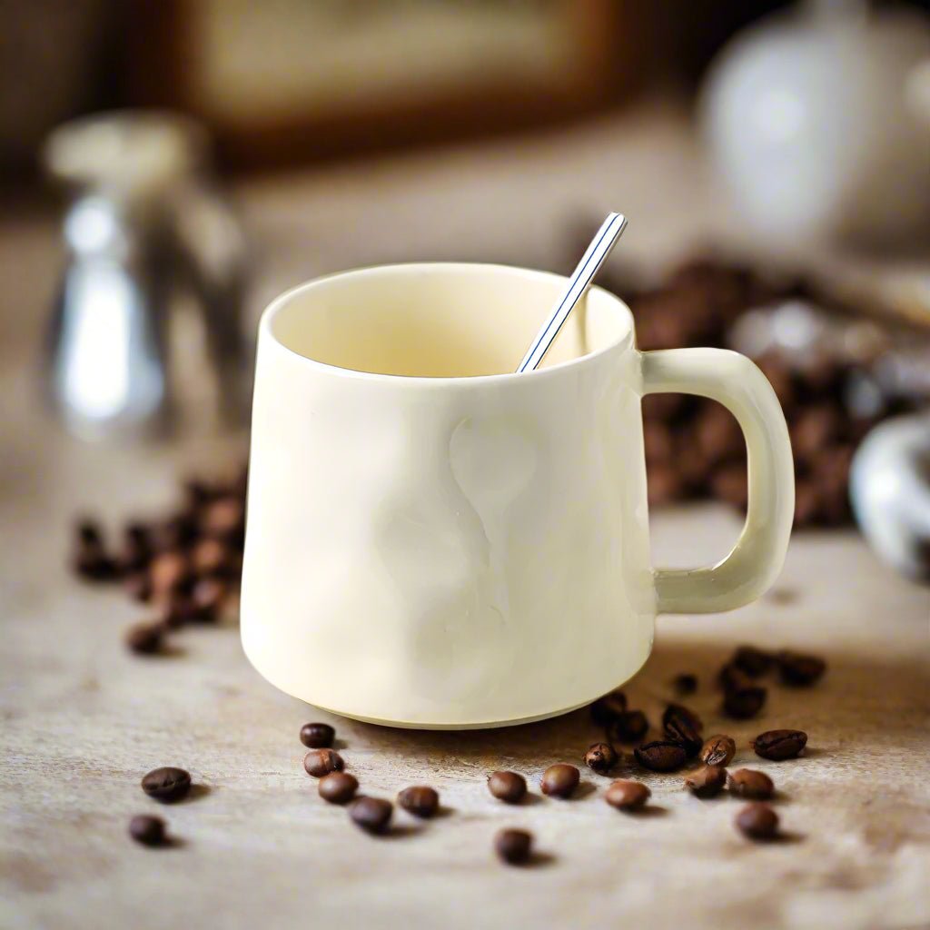 White mug with a spoon on a wooden surface surrounded by coffee beans