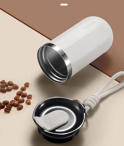 White tumbler with silver interior on a beige surface with coffee beans.
