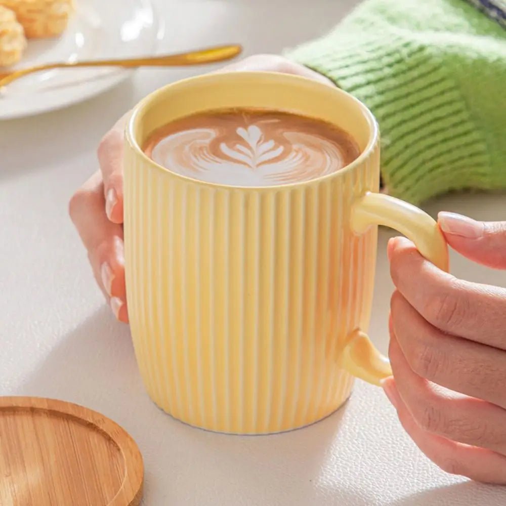 Yellow mug with striped pattern holding a cup of coffee, on a light surface.