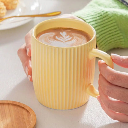 Yellow mug with striped pattern holding a cup of coffee, on a light surface.