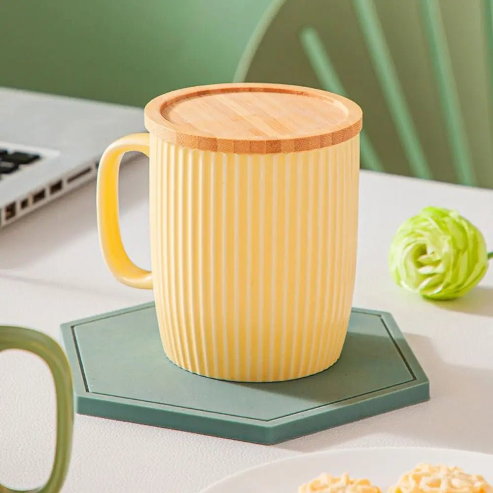 Yellow mug with wooden lid on a green coaster, laptop and snacks in the background